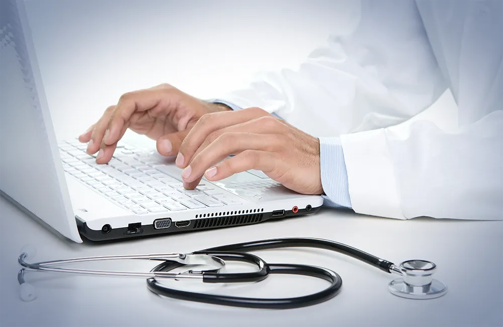 Médico con bata blanca y logo de Hospital Angeles recargado sobre un módulo y de fondo el área de Check up.
