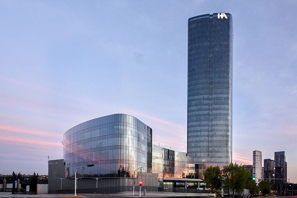 Edificio de cristal azul de 22 pisos y el atardecer de fondo.