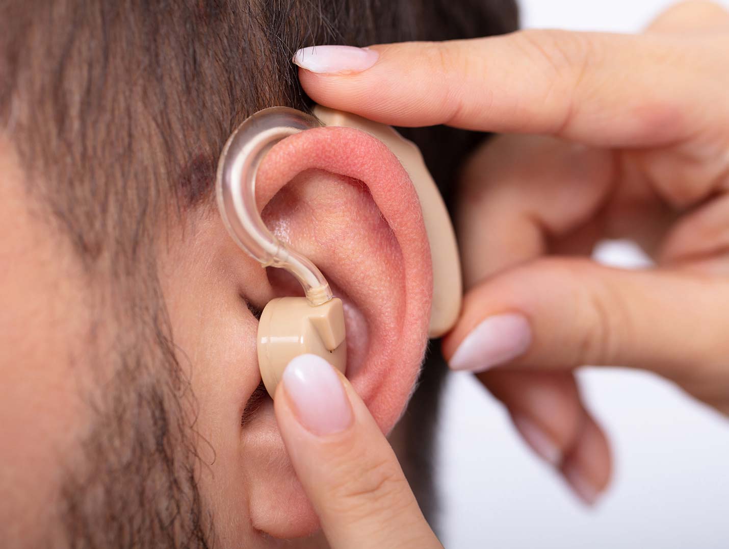 Una mano colocando un aparato auditivo de color café en la oreja de un paciente