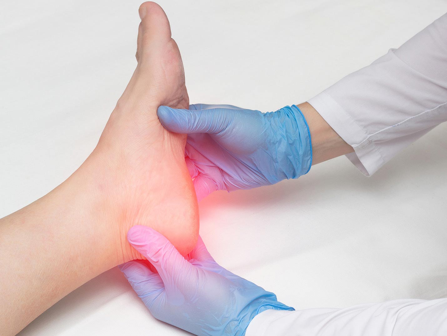Manos de un médico con guantes azules, sosteniendo el pie de un paciente. La zona del talón tiene una luz roja, indicando dolor