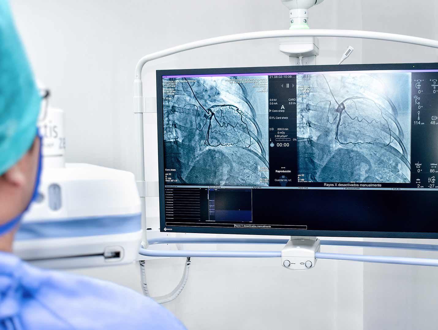 Doctora con pijama azul para cirugía, gorro y cubrebocas, observando una radiografía de tórax en un monitor blanco