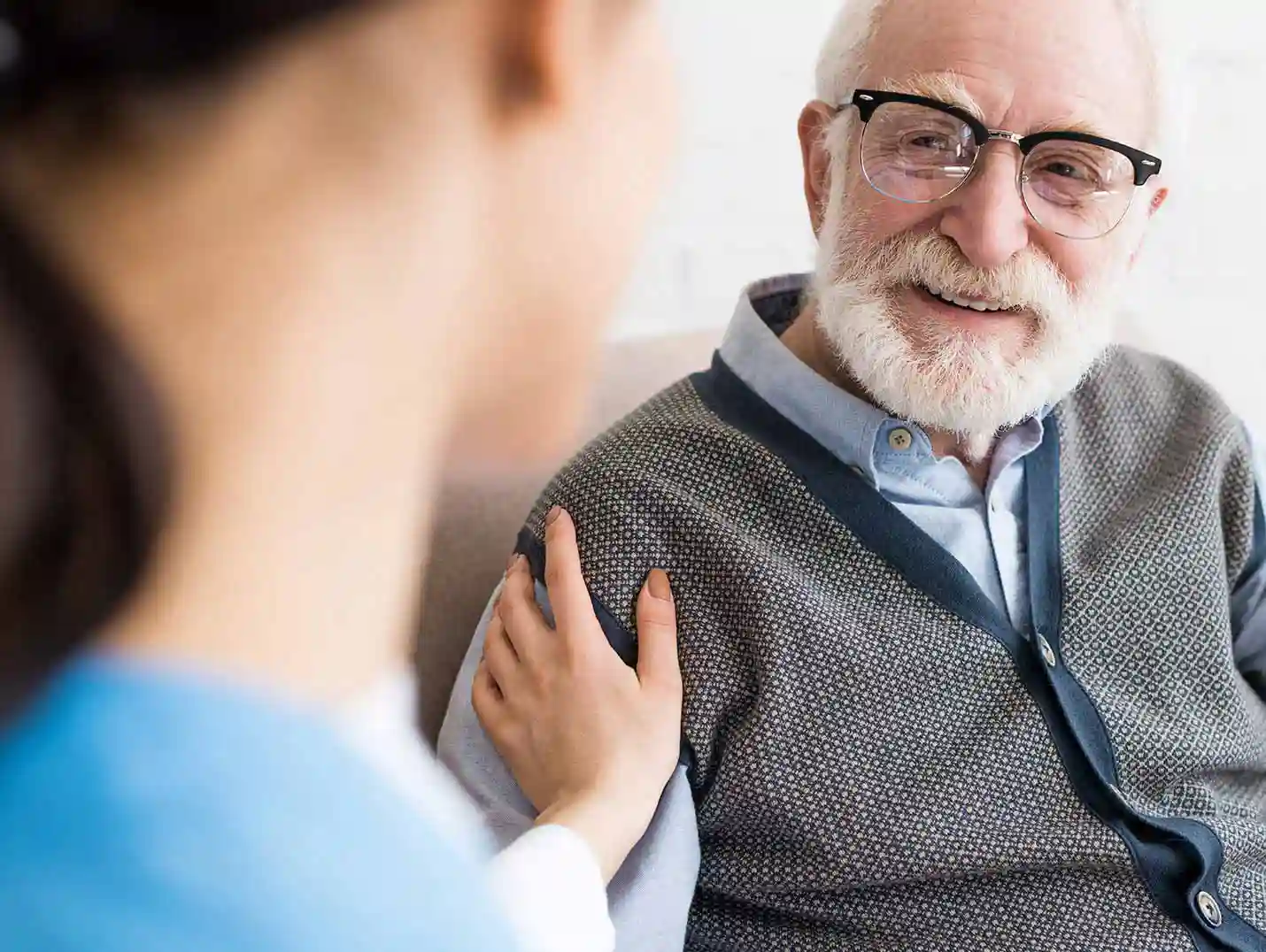 Doctora tocando el hombro derecho de un paciente de la tercera edad que viste con una camisa azul y chaleco gris