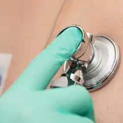 Mano de un médico con un guante verde, colocando el estetoscopio en el pecho de un paciente