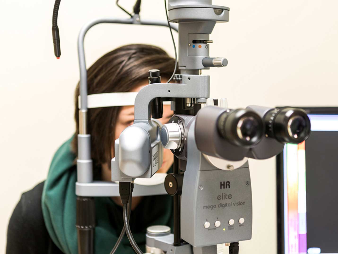 Paciente vestida con una blusa negra y bufanda verde, dentro de un consultorio para realizarse un examen oftalmológico