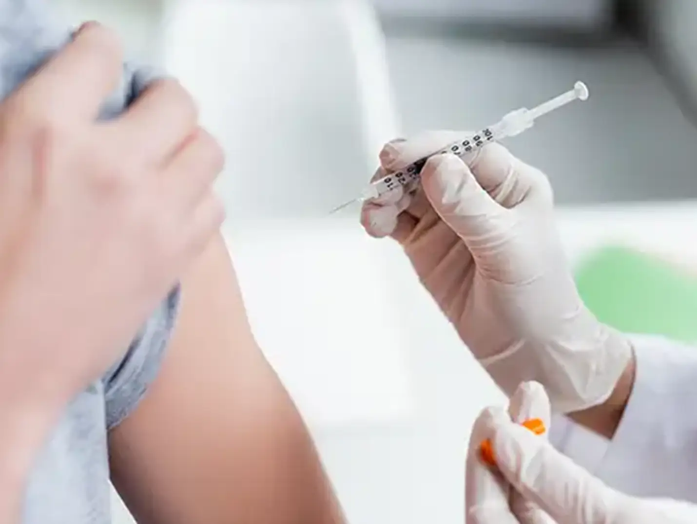  Médico con guantes blancos y jeringa en la mano, aplicando una vacuna en el brazo izquierdo de un paciente con playera gris.