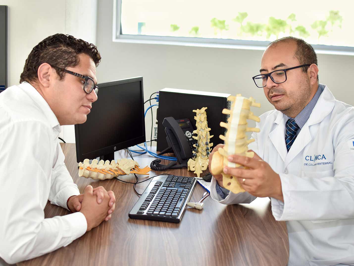 Doctor mostrándole un prototipo de una columna vertebral a un paciente que observa detenidamente