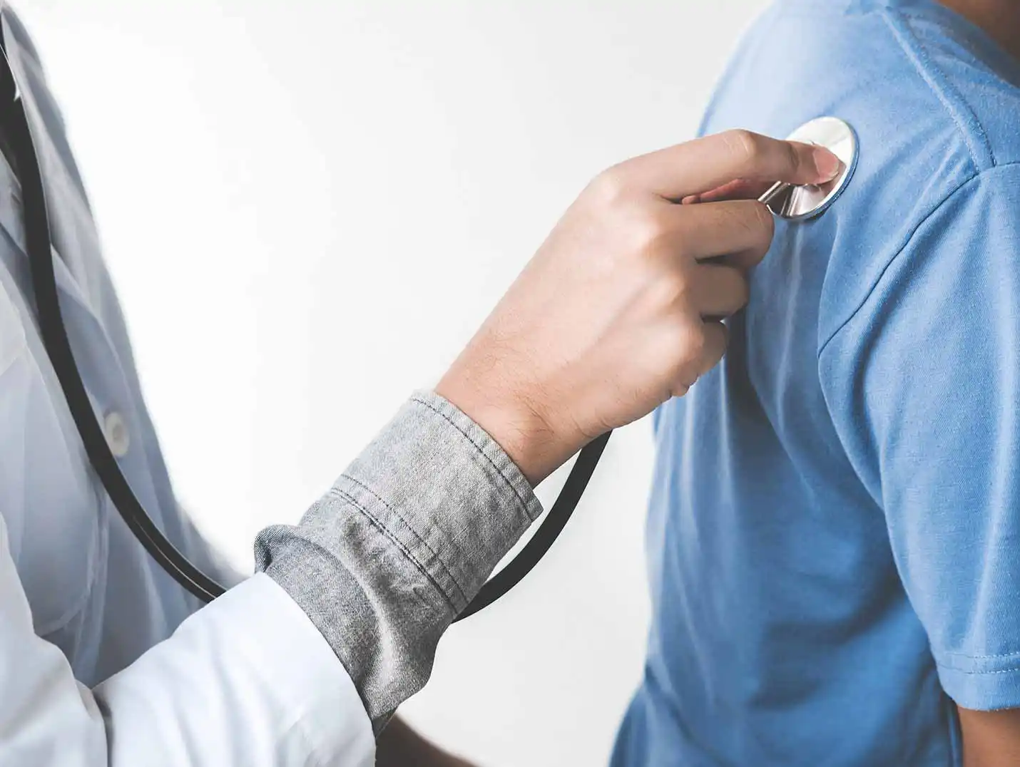 Mano de un doctor colocando el estetoscopio en el lado derecho de la espalda de un paciente que viste playera azul