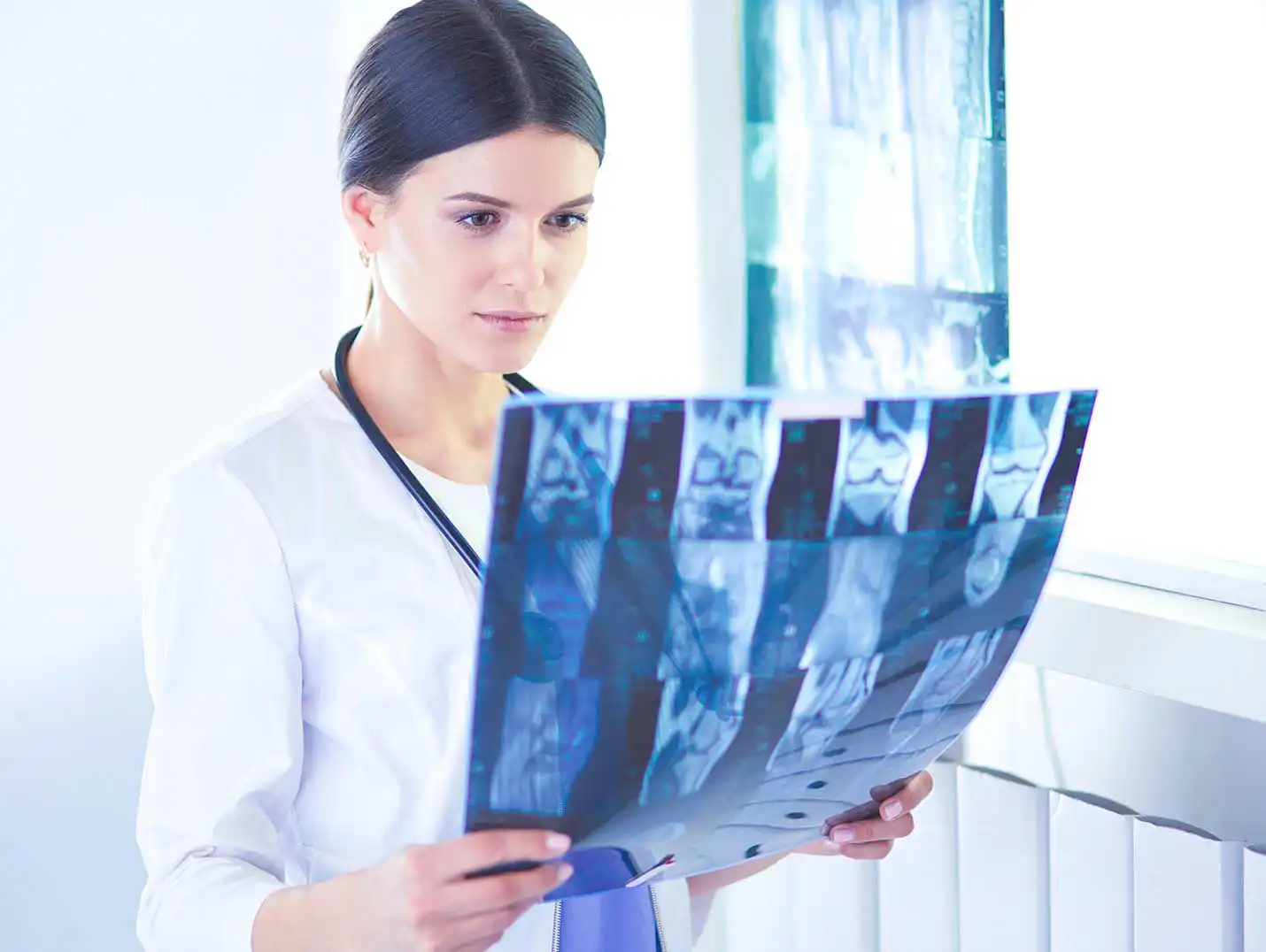 Doctora con bata blanca sosteniendo con sus manos una radiografía.