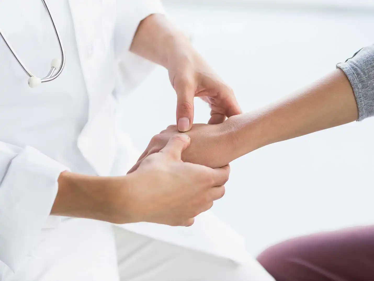 Médico con bata blanca y un estetoscopio, tomando la mano derecha de una paciente