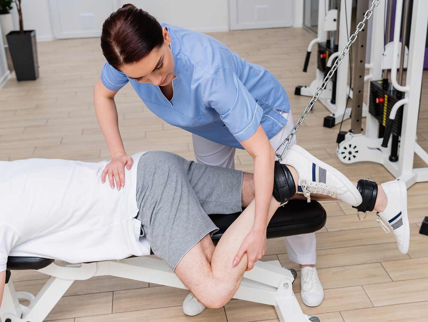 Doctora ayudando a un paciente a realizar ejercicios de rehabilitación a su pierna izquierda con un equipo de gimnasio