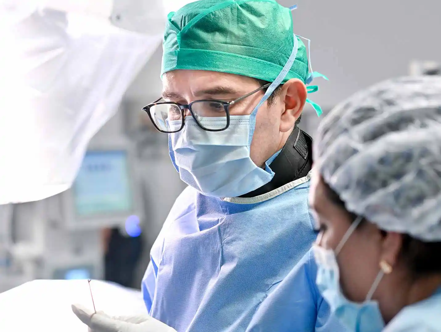 Dos médicos en un quirófano, vestidos con pijamas para cirugía azules, gorro, cofia, cubrebocas y guantes blancos