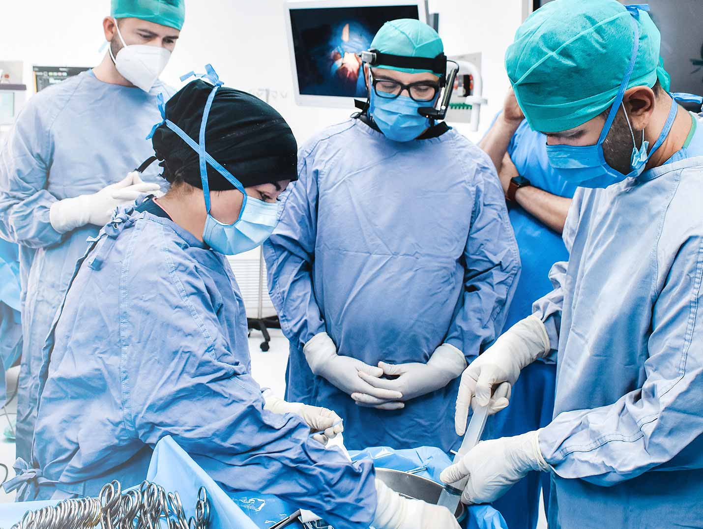 Médicos con pijama quirurgica y gorros dentro de un quirófano durante un procedimiento.