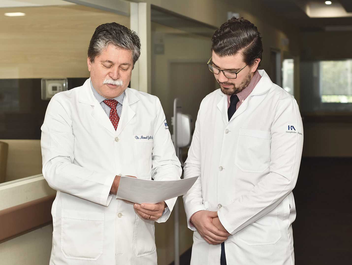 Dos médicos de Hospital Angeles con batas blancas, viendo detenidamente unos documentos que uno de ellos tiene en sus manos