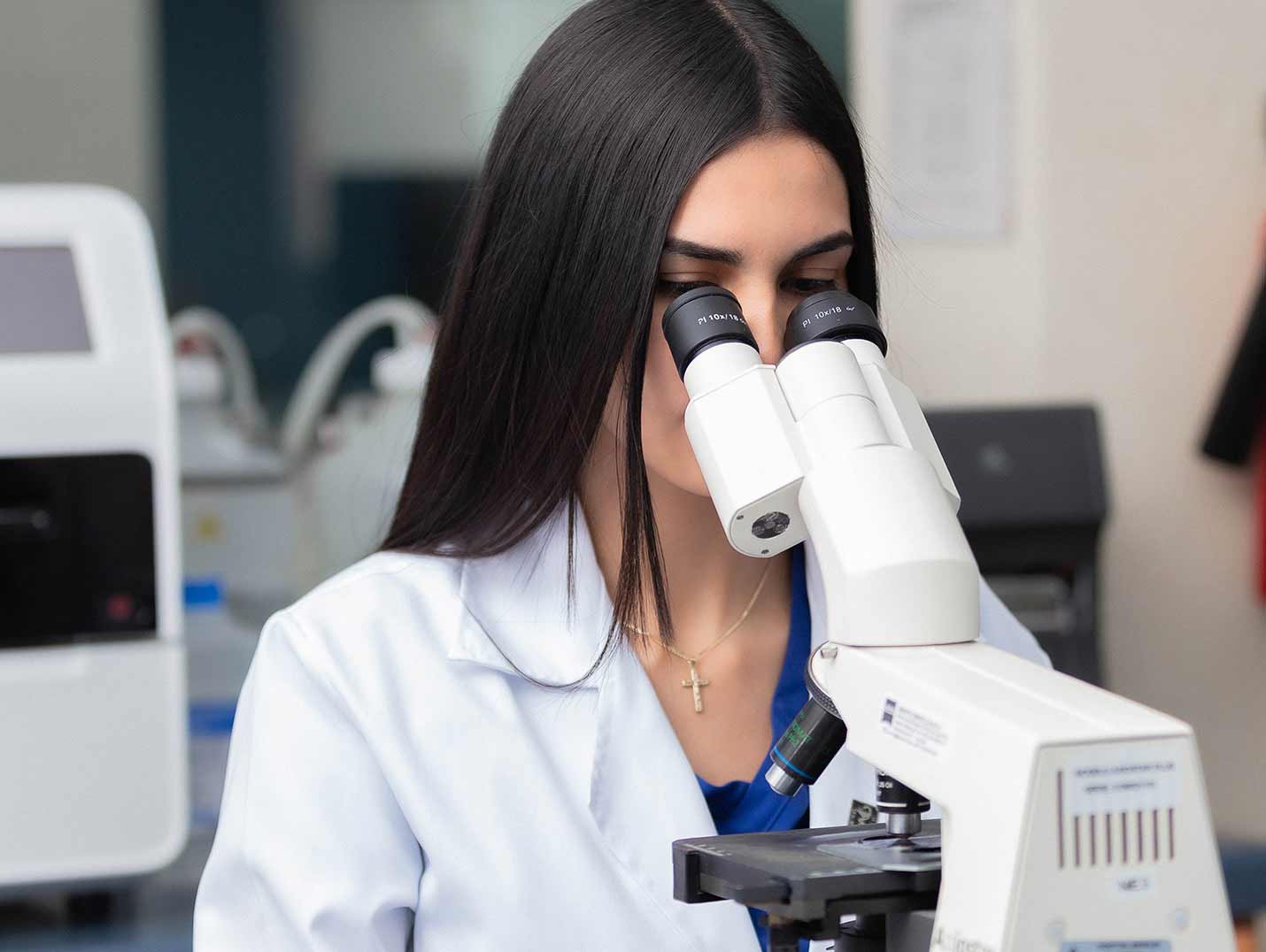 Doctora con bata blanca observando una muestra de laboratorio a través de un microscopio de color blanco