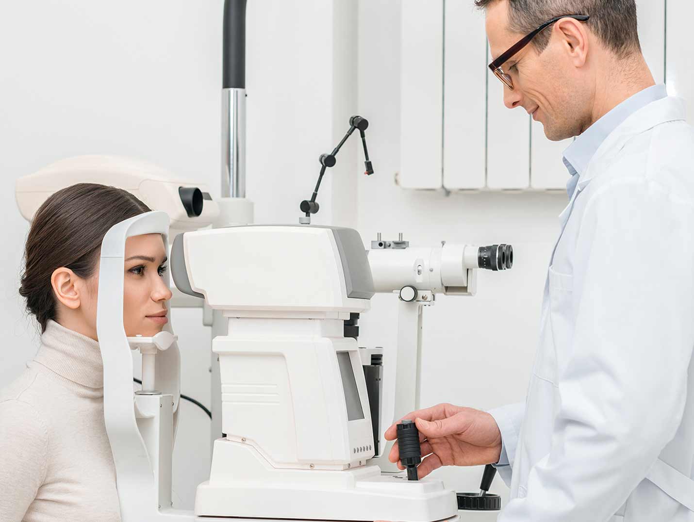 Doctor con bata blanca realizando un examen oftalmológico a una paciente que viste un suéter de cuello alto blanco