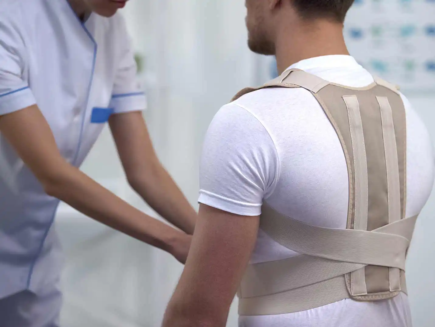 Enfermero vistiendo uniforme blanco, ajustando una faja de soporte lumbar a un paciente que está sentado