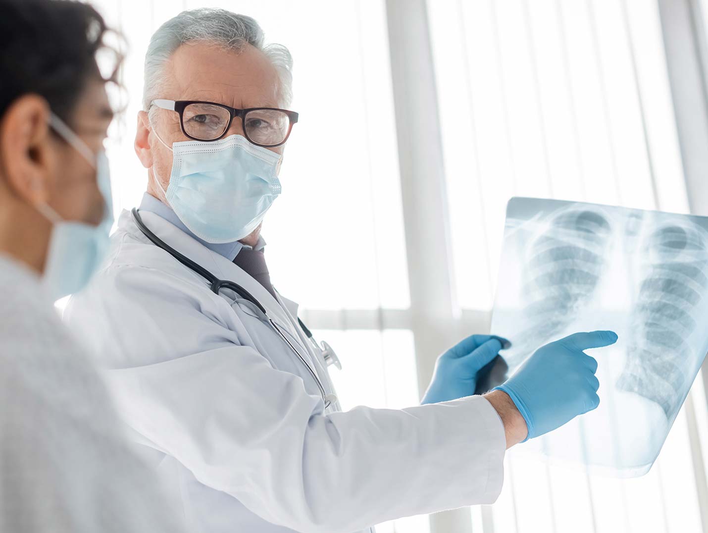 Doctor con bata blanca y guantes azules, sosteniendo y mostrándole a otra doctora una radiografía de tórax