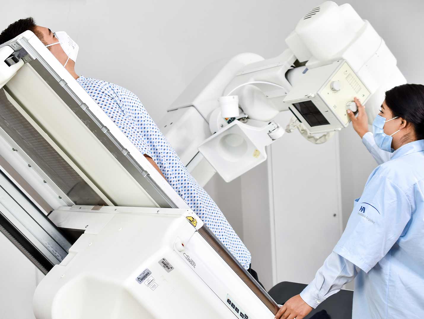 Paciente recostado en la camilla del sistema de rayos X para realizarse un estudio de imagen. A su lado está una doctora