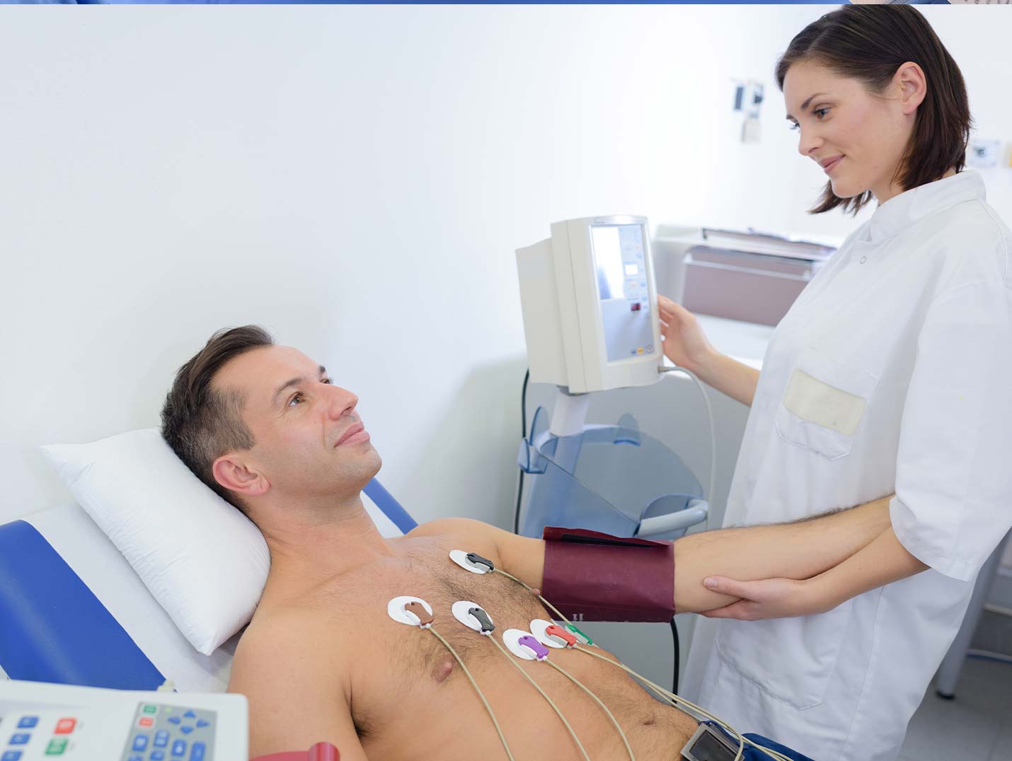 Paciente sin camisa recostado en una silla reclinable, con seis electrodos en su pecho, mientras un médico le toma la presión