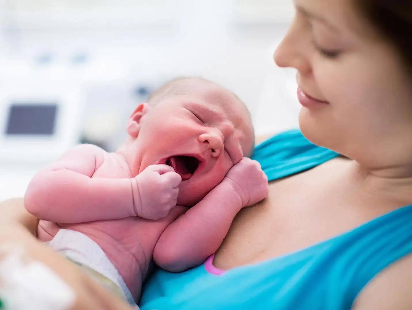 Una mamá sonriente cargando y mirando a su bebé recién nacido que está bostezando