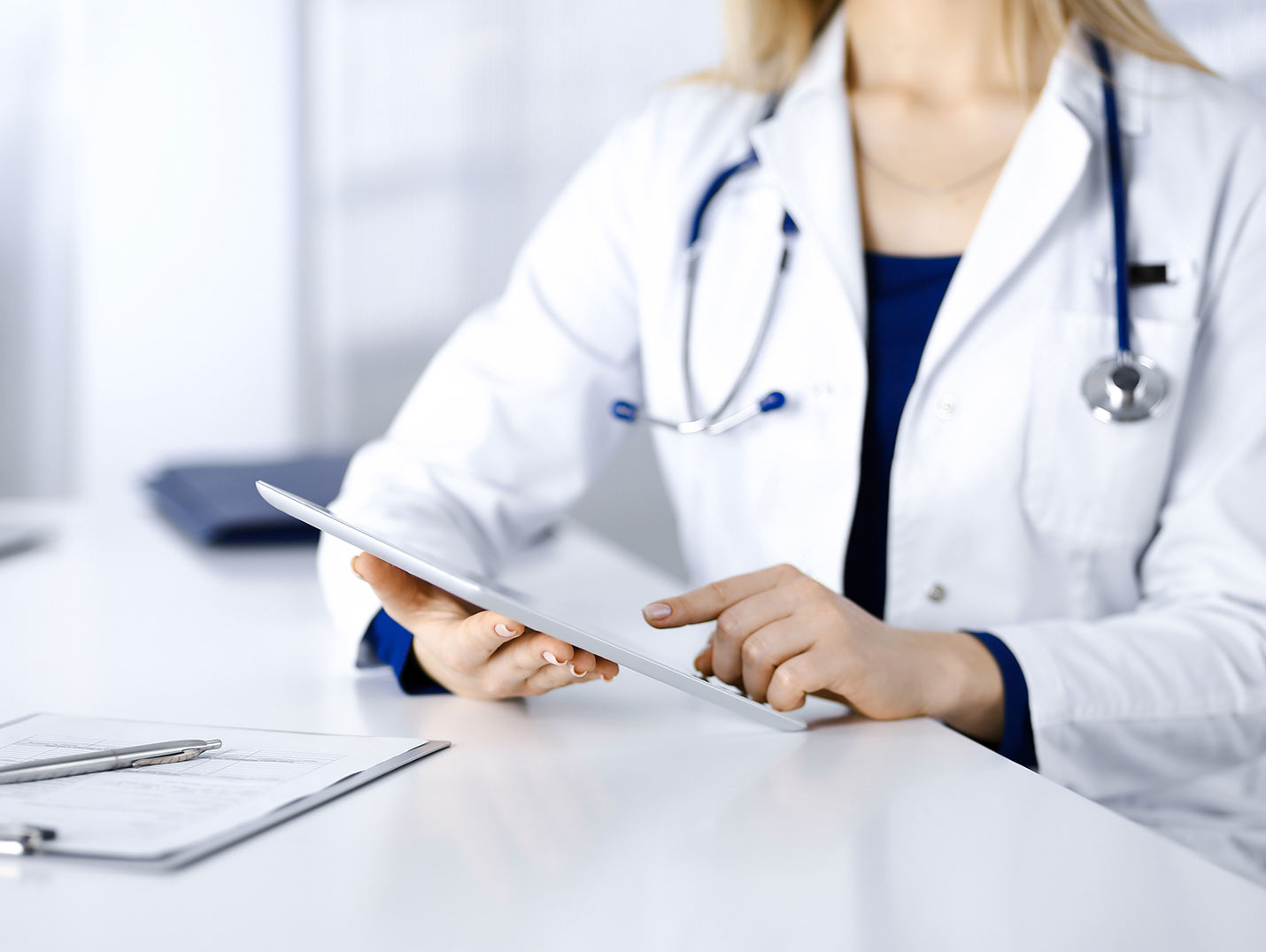 Doctora con bata blanca, sosteniendo y revisando su ipad en un consultorio médico