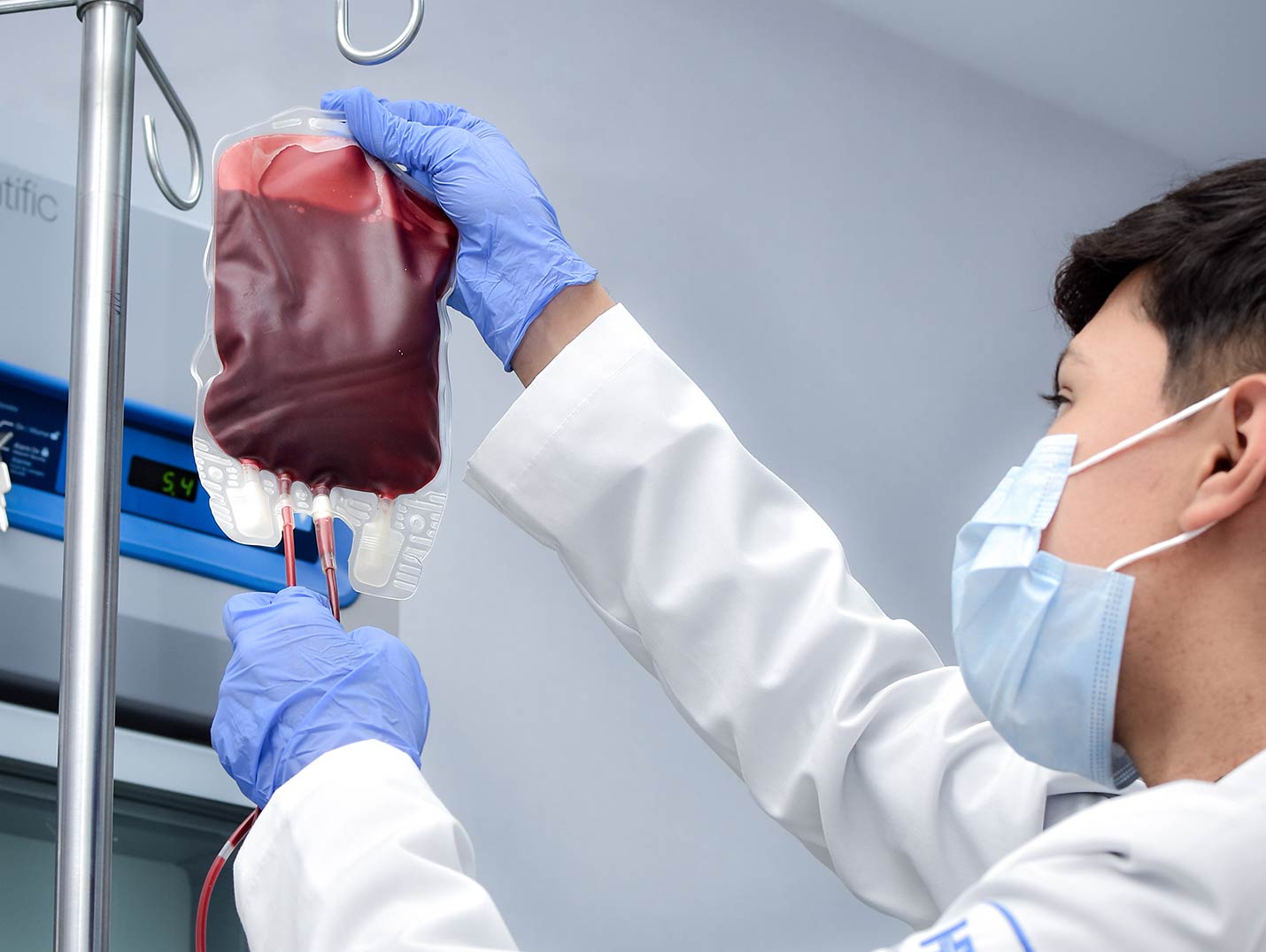Doctor de Hospital Angeles con bata blanca y guantes azules, colocando una bolsa de transfusión sanguínea en un porta sueros