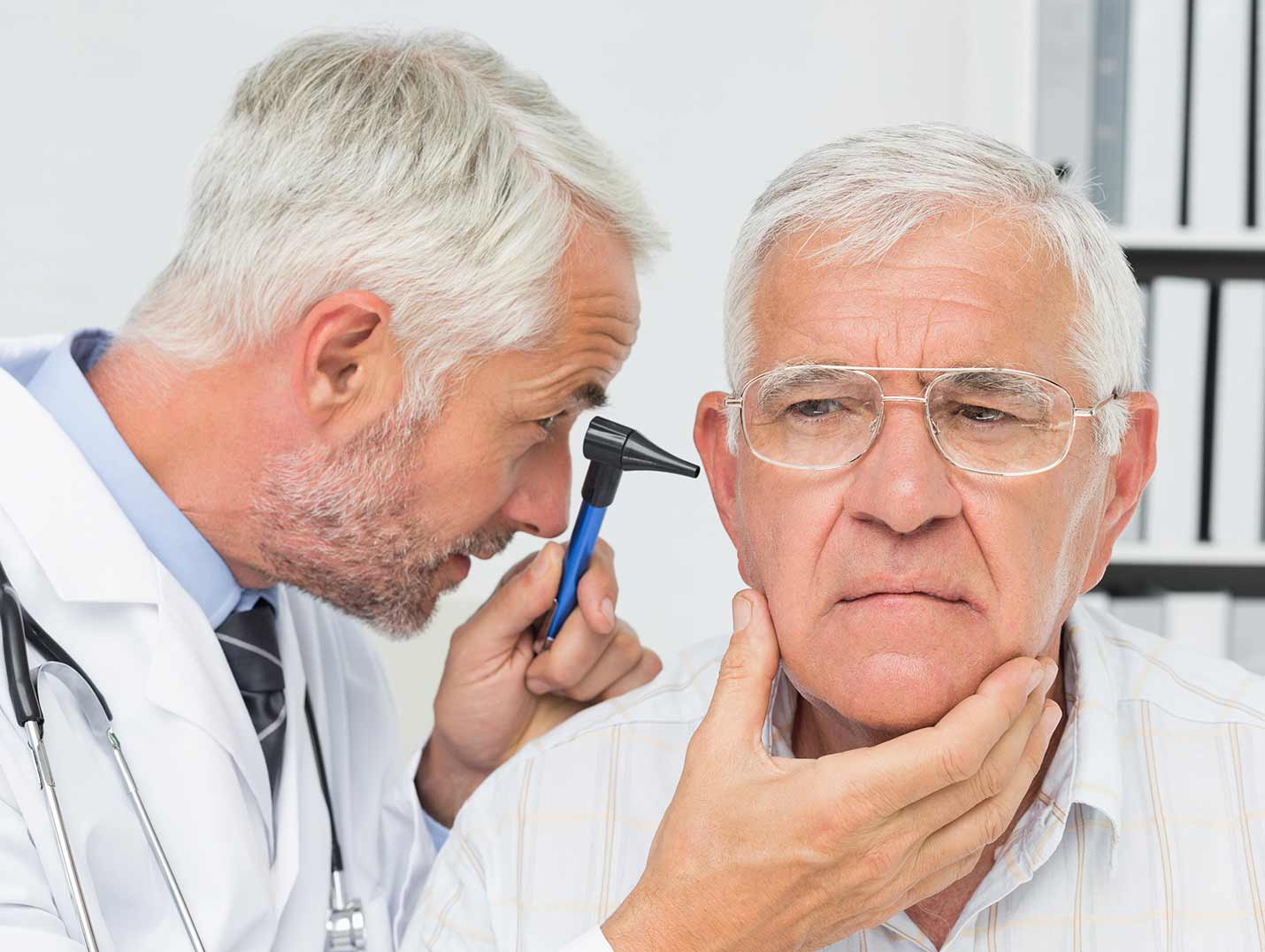 Doctor con bata blanca, examinando el oído derecho de un paciente de la tercera edad con un otoscopio
