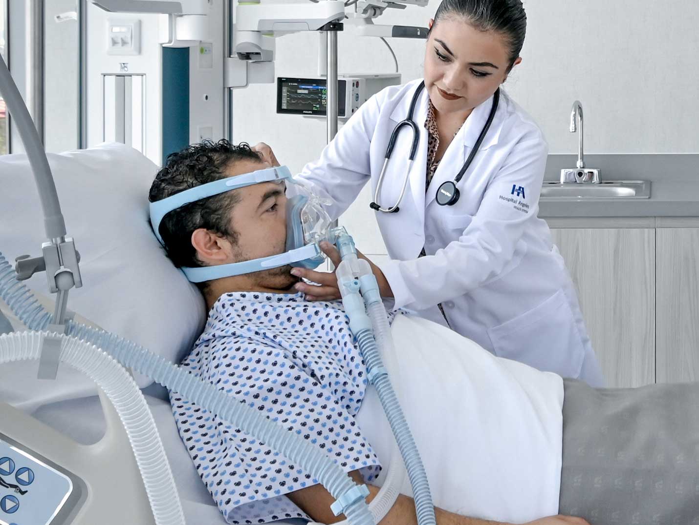Doctora de Hospital Angeles con una bata blanca, colocando una máscara de oxígeno a un paciente que se encuentra internado