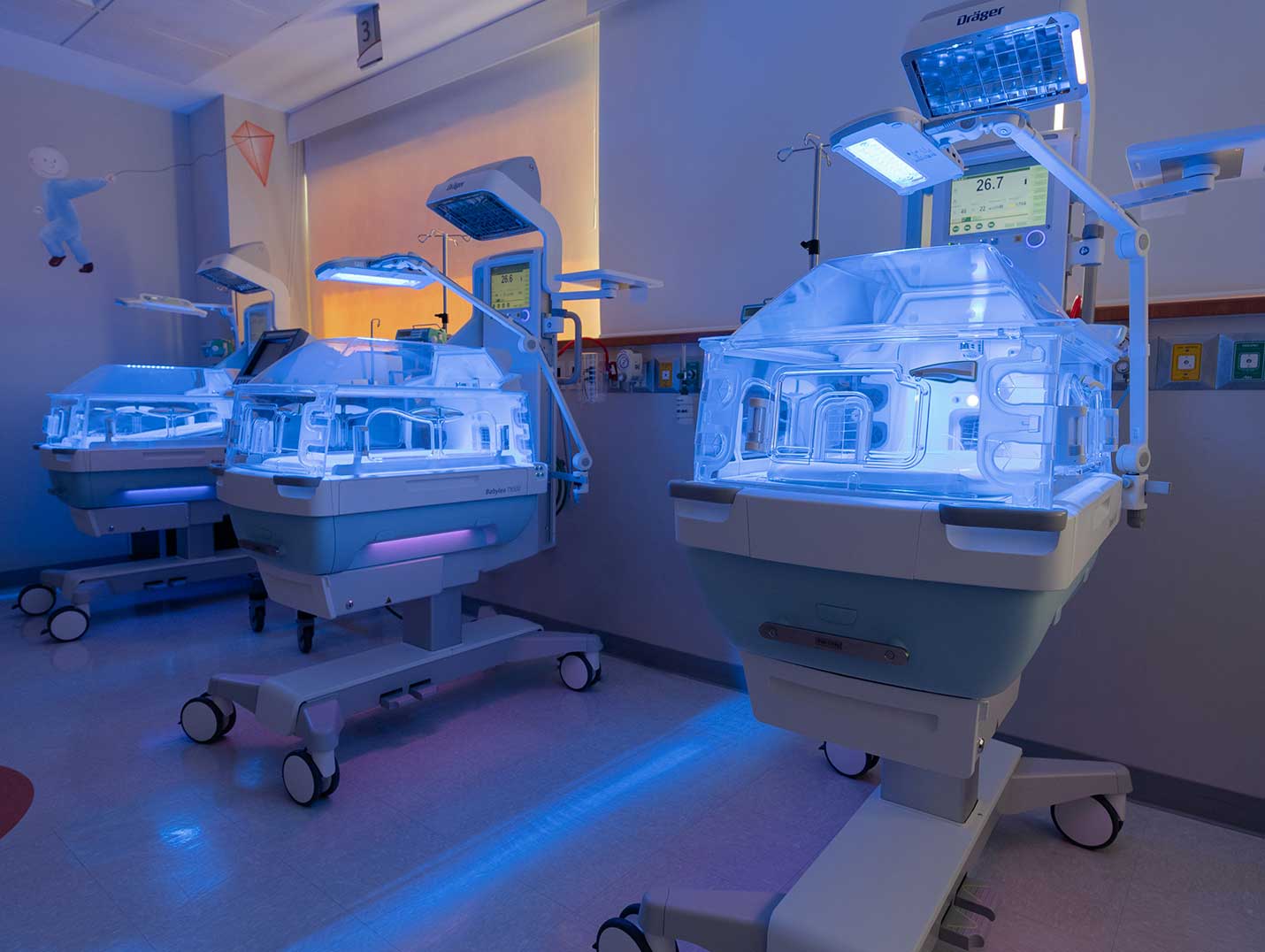 Área de terapia intensiva neonatal con una incubadora de color blanco y azul, alumbrada con luz de color azul
