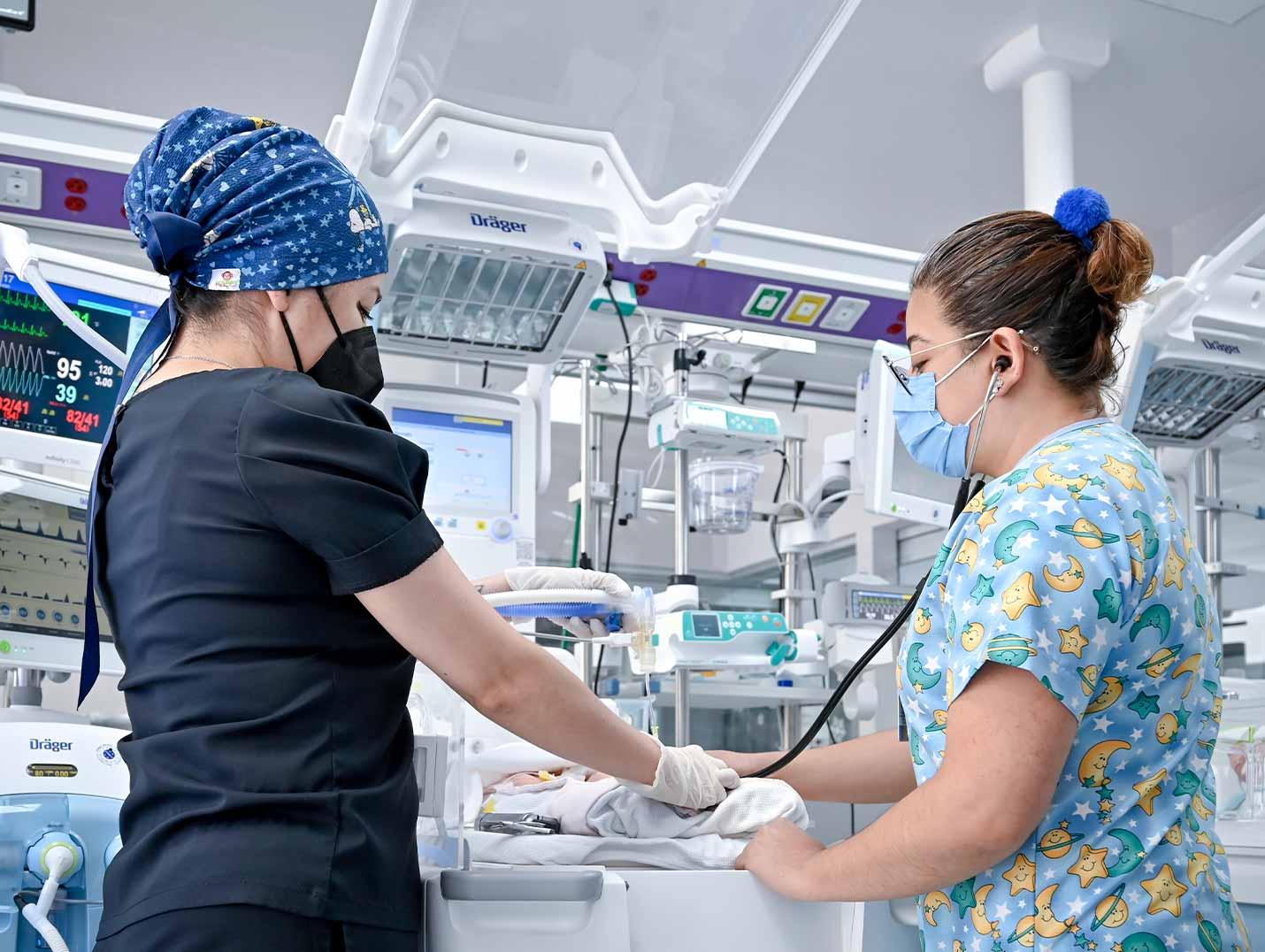Dos doctoras en la sala de terapia intermedia neonatal. Una de ellas está escuchando los latidos del corazón de un recién nacido