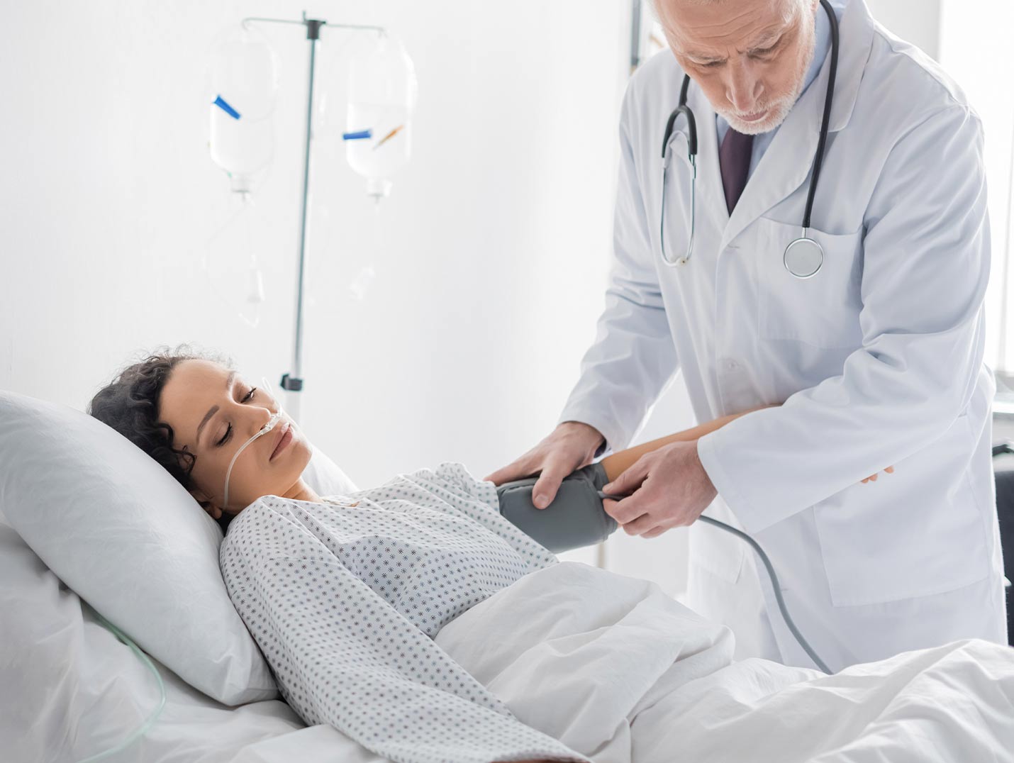 Doctor con bata blanca tomando la presión arterial de la paciente que se encuentra recostada en una cama de hospital 
