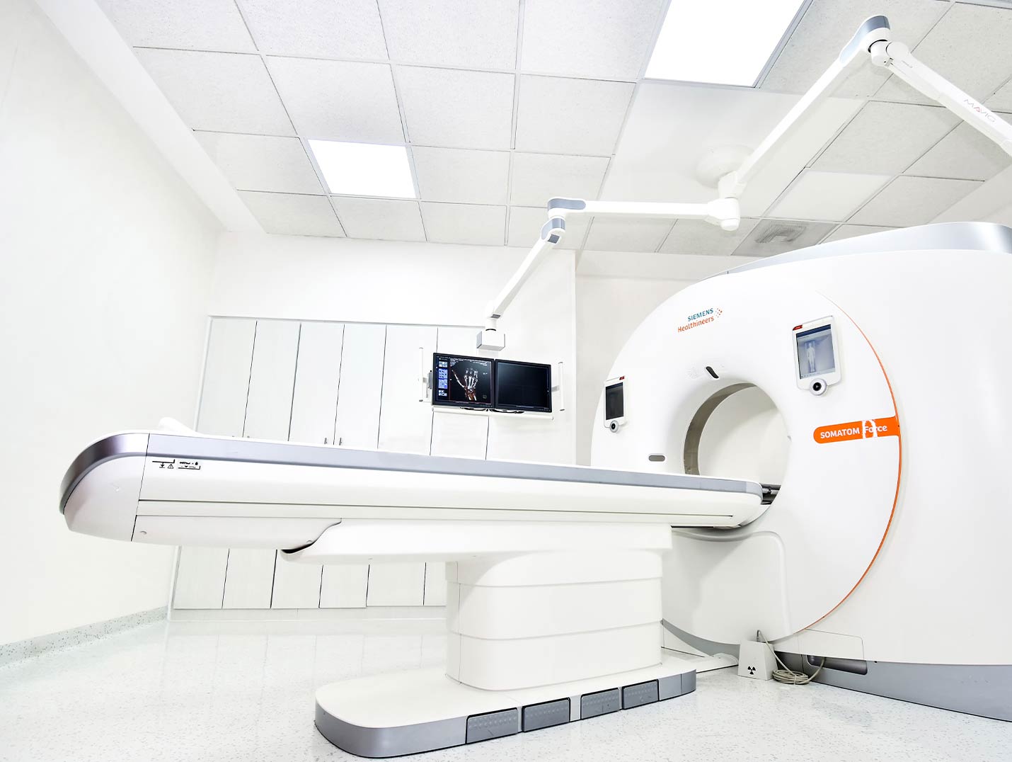 Cuarto amplio con el equipo de tomografía de color blanco con un monitor que muestra una radiografía