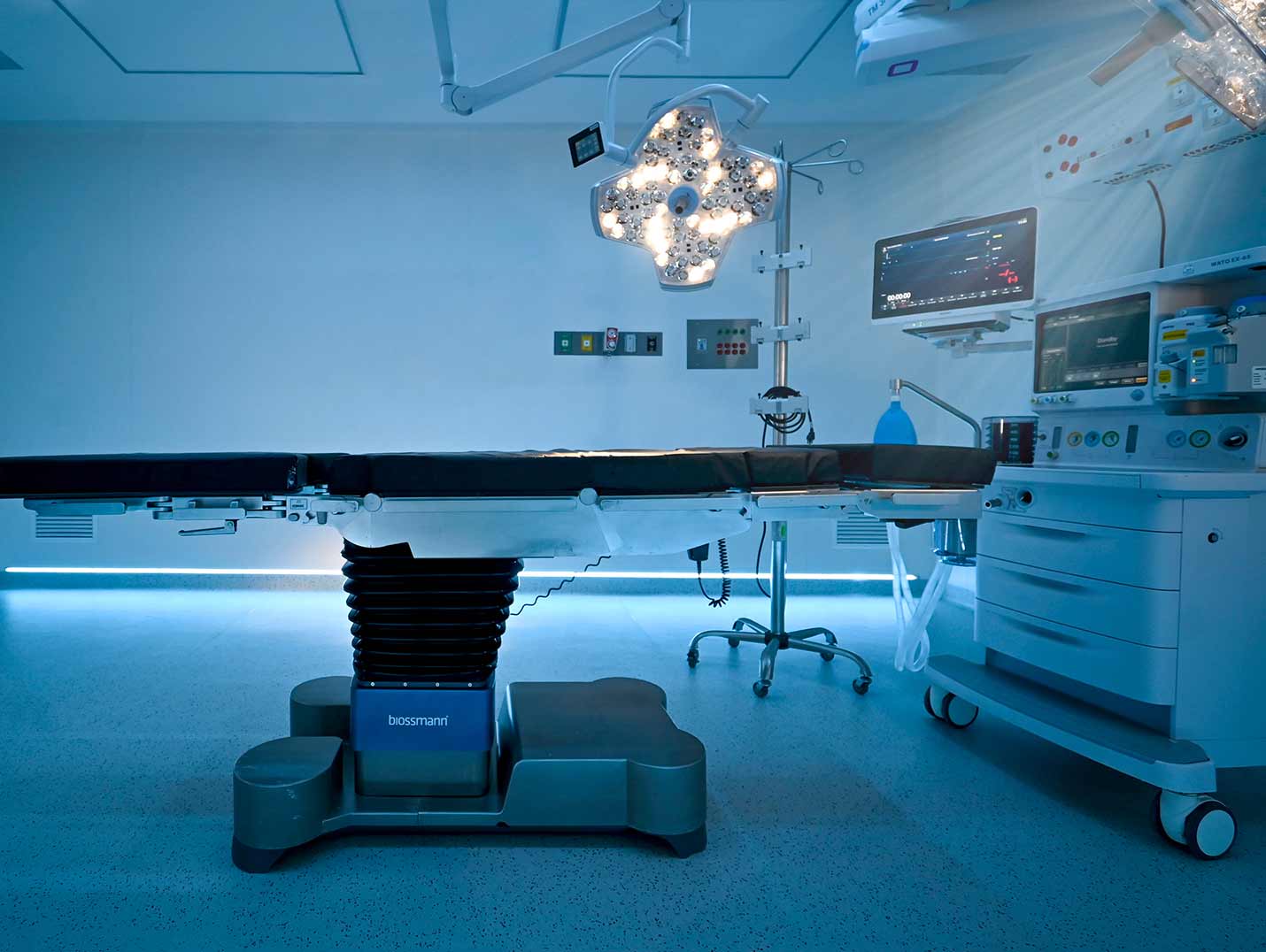 Quirófano inteligente con camilla quirúrgica, dos lámparas LED, monitor y equipo de anestesia, iluminado con una luz azul