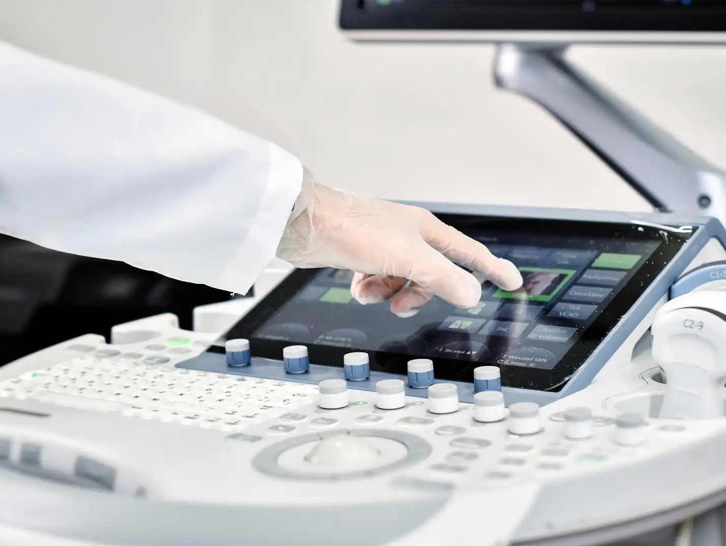 Médico con bata blanca y guantes transparentes presionando un comando del aparato voluson para ultrasonido.