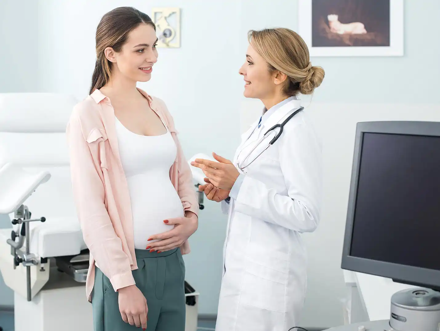 Paciente embarazada tocandose el vientre mientras una doctora frente a ella le explica sobre un estudio.