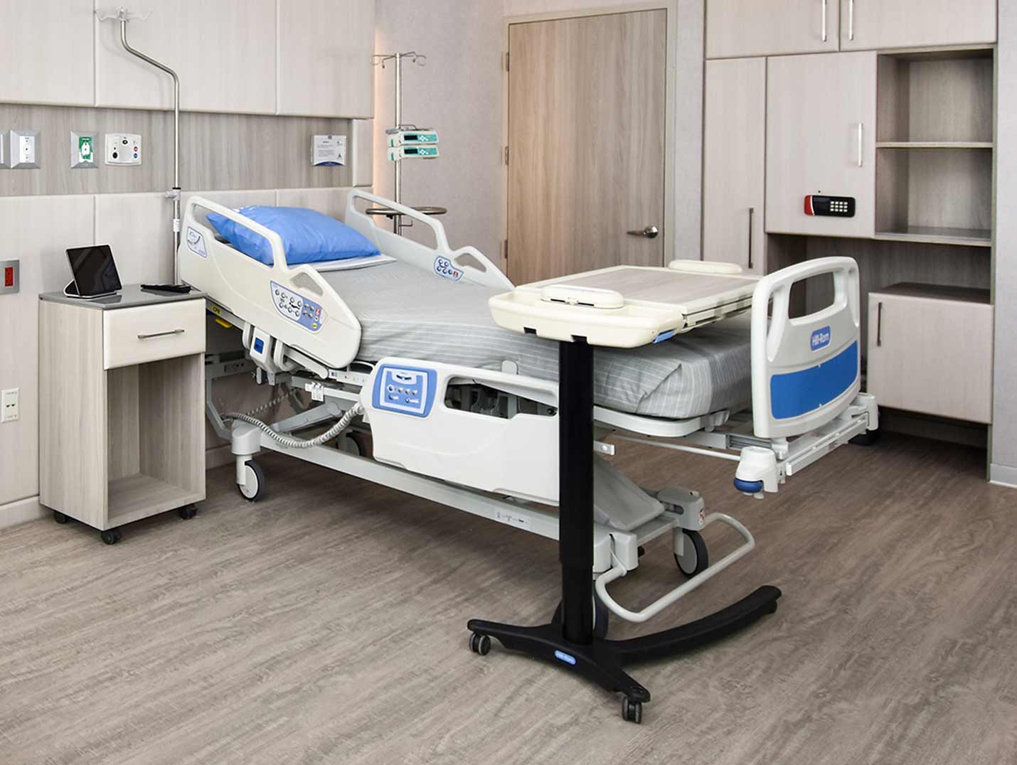 Habitación hospitalaria pintada en tonos grises, con una cama cubierta con una sábana gris y una almohada azul encima