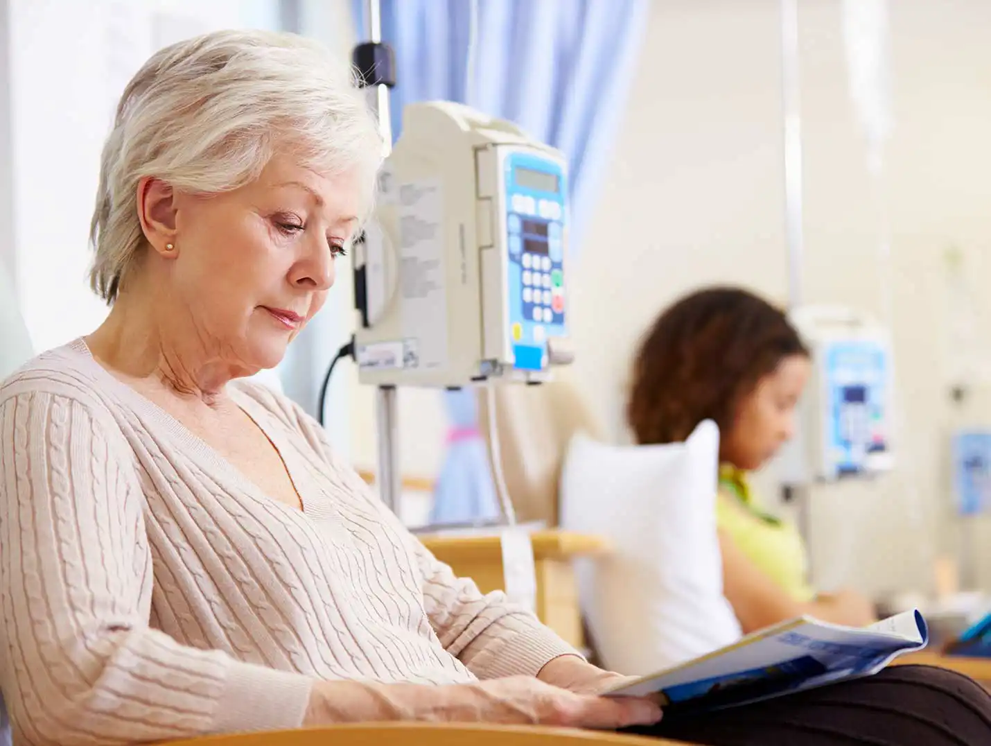 Paciente de la tercera edad sentada y leyendo una revista mientras recibe su tratamiento de quimioterapia