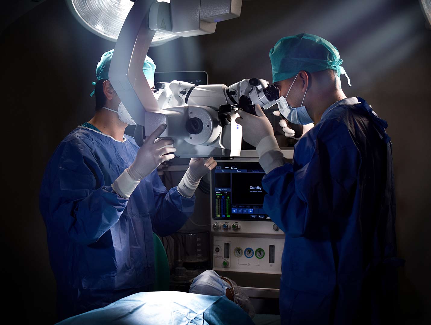 Dos médicos con pijamas azules para cirugía, gorros verdes y guantes blancos, realizando un procedimiento quirúrgico