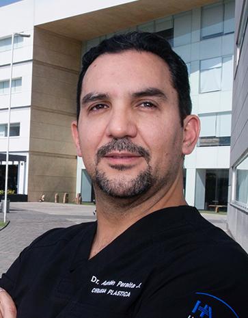 Es la foto de un cirujano plástico en Ciudad de México de Hospital Angeles. Utiliza un uniforme negro con su nombre bordado en letras blancas del lado izquierdo de su pecho y en brazo del mismo lado del mtiene bordado el logotipo del hospital. El fondo de la imagen es el frente del hospital.