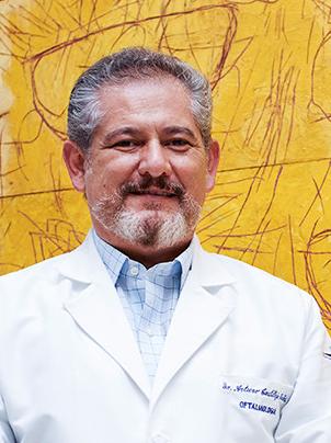 Es la foto de perfil de un oftalmólogo en Ciudad de México de Hospital Angeles Lindavista. Tiene el bigote negro, además de barba y cabello gris. Usa una bata blanca con una camisa azul.