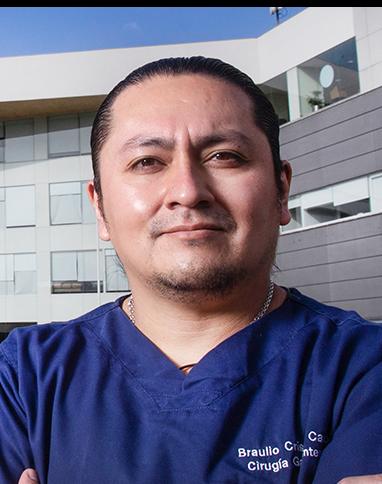 Es la foto de perfil de un endoscopista especializado en cirugía general y gastrocirugía en Ciudad de México de Hospital Angeles. Viste un uniforme azul marino con una cadena plateada, tiene el cabello peinado hacia atrás. De fondo se encuentra el hospital. 