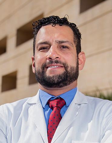 Es la foto de perfil de un cardiólogo en Ciudad de México de Hospital Angeles. Tiene una bata blanca, camisa azul y corbata roja, tiene barba, bigote y cejas pobladas, su cabello es rizado.