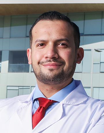 Es la foto de perfil de un ortopedista y traumatólogo en Ciudad de México de Hospital Angeles. Viste una bata blanca con camisa azul cielo y corbata roja brillante. Está sonriendo sutilmente a la cámara, es de tez blanca, tiene bigote y barba.