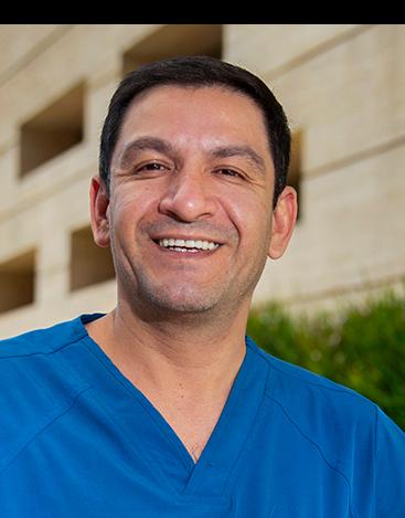 Es la foto de perfil de un cirujano general en Ciudad de México de Hospital Angeles. Tiene un uniforme azul rey, está sonriendo a la cámara, es de tez morena y cabello oscuro.