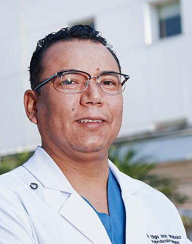 Es la foto de perfil de un ginecólogo y obstetra en Ciudad de México de Hospital Angeles Lindavista. Tiene el cabello negro. Usa lentes, una bata blanca y un uniforme médico azul.