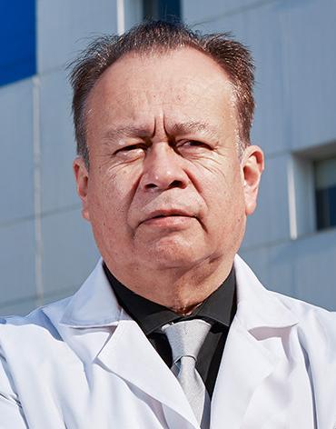 Es la foto de perfil de un cirujano oncológico en Ciudad de México de Hospital Angeles Lindavista. Tiene el cabello café. Usa una bata blanca, una camisa negra y una corbata gris.