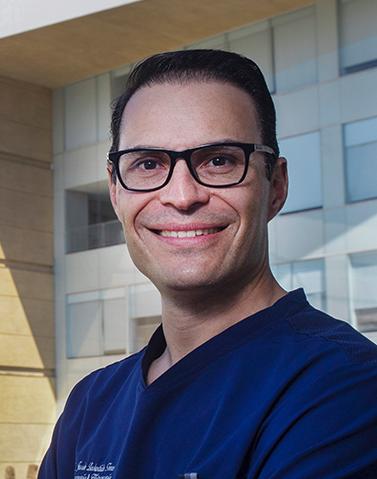 Es la foto de perfil de un ginecólogo y obstetra en Ciudad de México de Hospital Angeles. Viste un uniforme azul rey, está sonriendo y tiene lentes con un contorno nnegro.