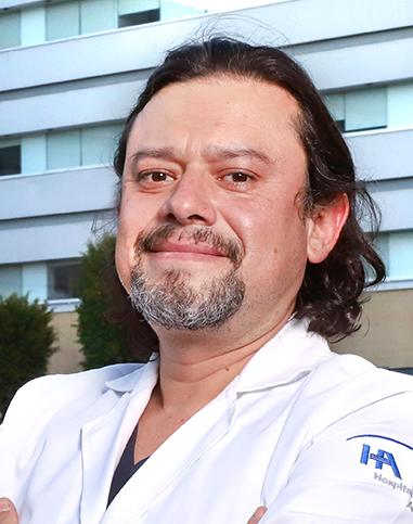 Es la foto de perfil de un cardiólogo en Ciudad de México de Hospital Angeles. El doctor tiene barba de candado, cabello ligeramente largo, viste una bata blanca y playera negra.