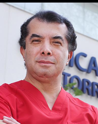 Es la foto de perfil de un gastrocirujano en Ciudad de México de Hospital Angeles Clínica Londres. Utiliza un uniforme rojo, tiene los brazo cruzados y sonríe suavemente. 