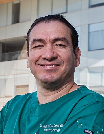 Es la foto de perfil de un endoscopista especialista en cirugía general en Ciudad de México de Hospital Angeles. Tiene un uniforme verde oscuro, está sonriendo, tiene cejas anchas y cabello oscuro. 